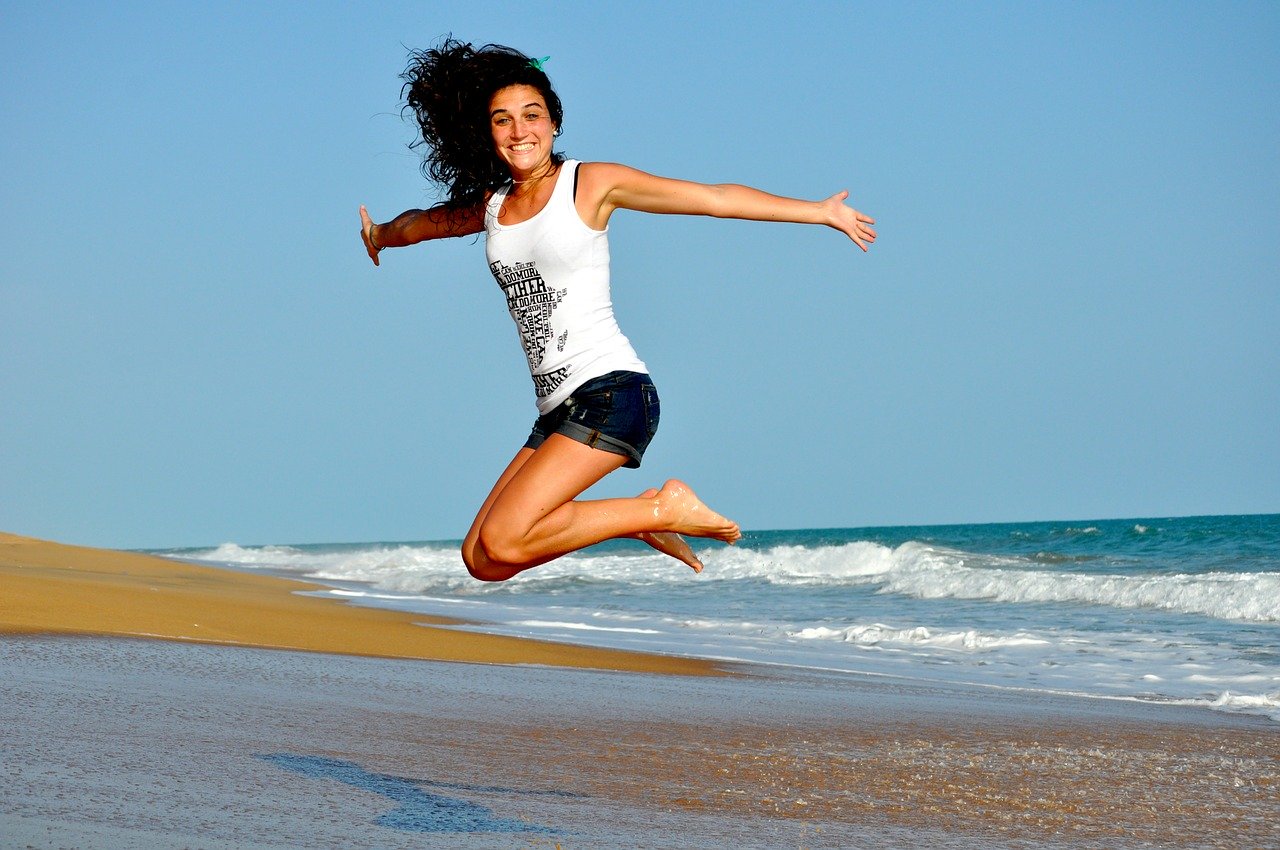 Una chica da un salto en una playa, ella está muy alegre, sonríe