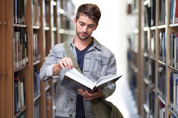 Un estudiante recorre una biblioteca con un libro en la mano